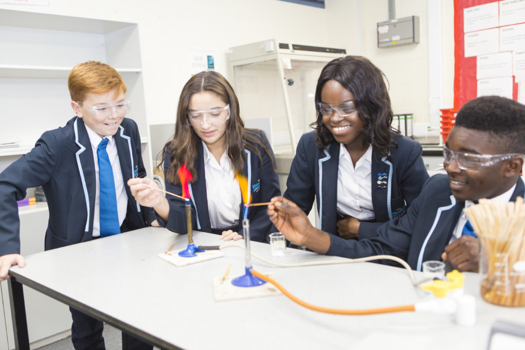 Four students are pictured collaborating to carry out an experiments involving Bunsen Burners in a Science Lab.