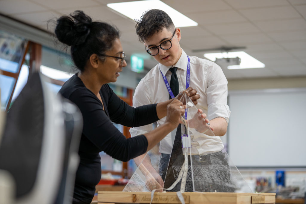 A member of staff is seen assisting a student to create a glass model he is building in a Design & Technology class.