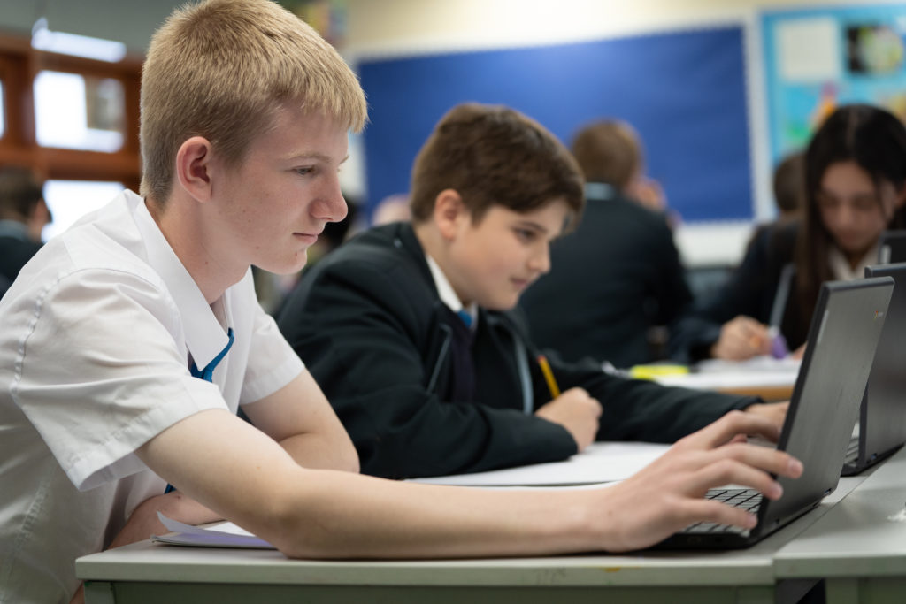 Two male students are pictured working individually on their laptop computers in a quiet space.