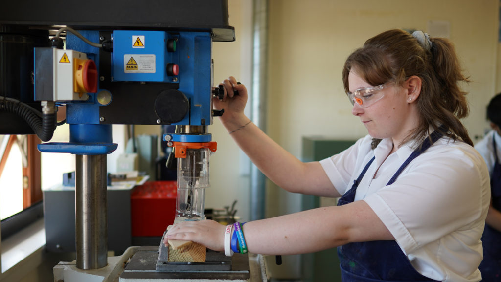 A female student is seen operating a large piece of machinery during a Design & Technology class.