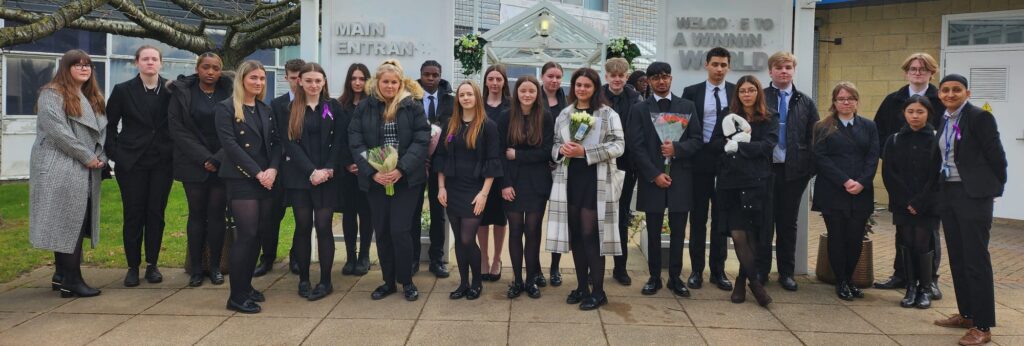 A large group of students are pictured standing alongside the Principal, holding flowers in their hands and posing for the camera.