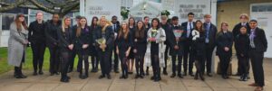 A large group of students are pictured standing alongside the Principal, holding flowers in their hands and posing for the camera.