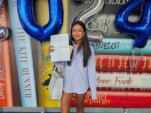 A female Post-16 student is seen smiling for the camera, whilst holding up her A-Level results.
