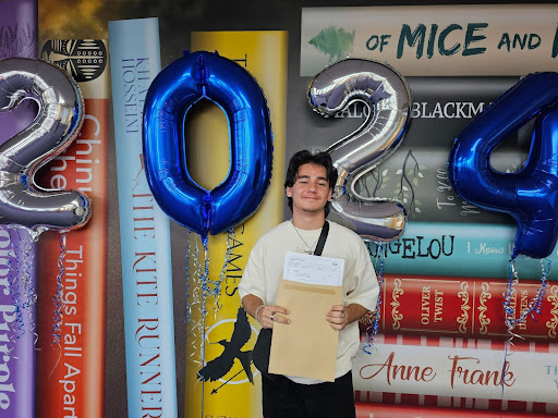 A male Post-16 student is seen smiling for the camera, whilst holding up his A-Level results.